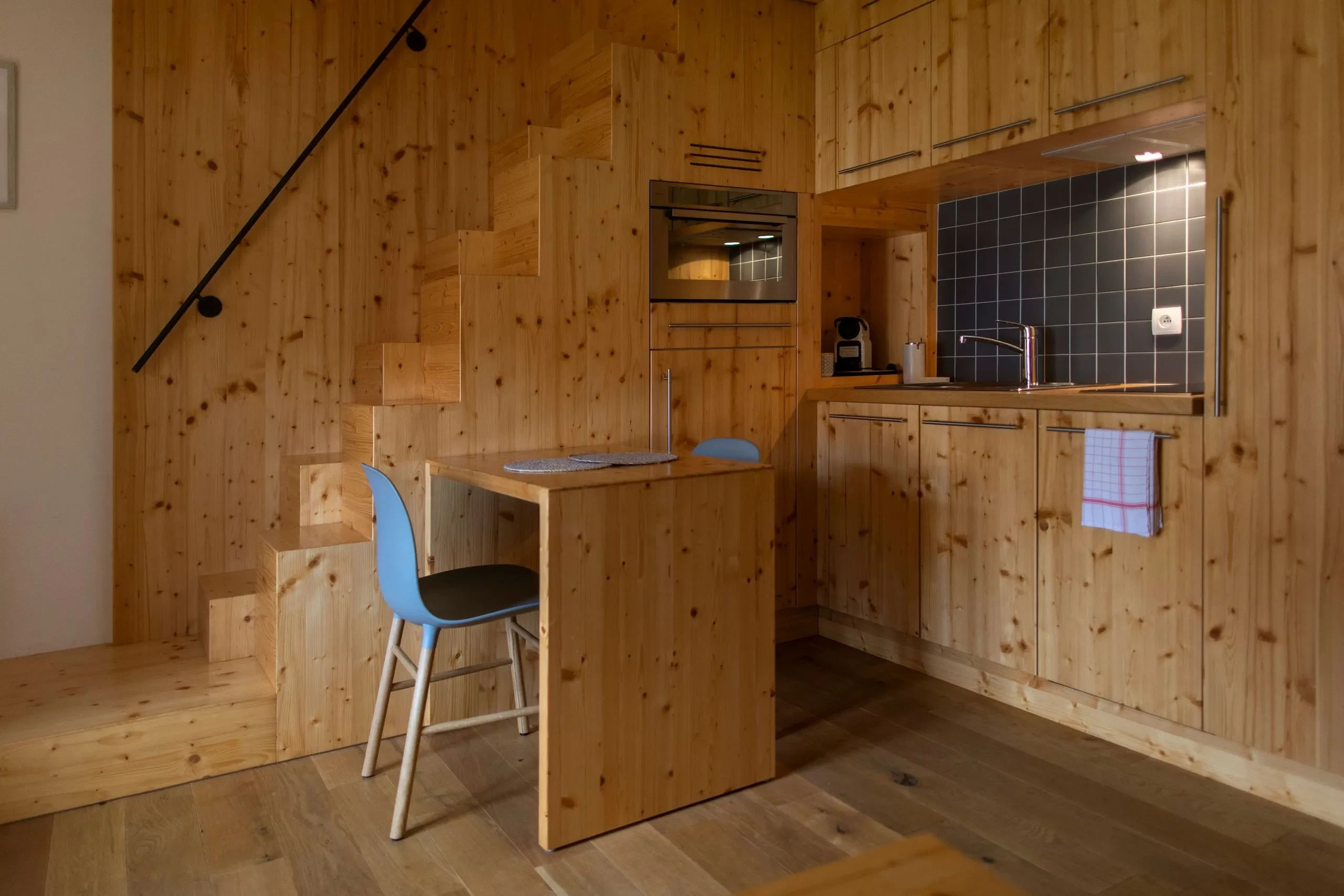 Wooden kitchen with stairs and blue chair.