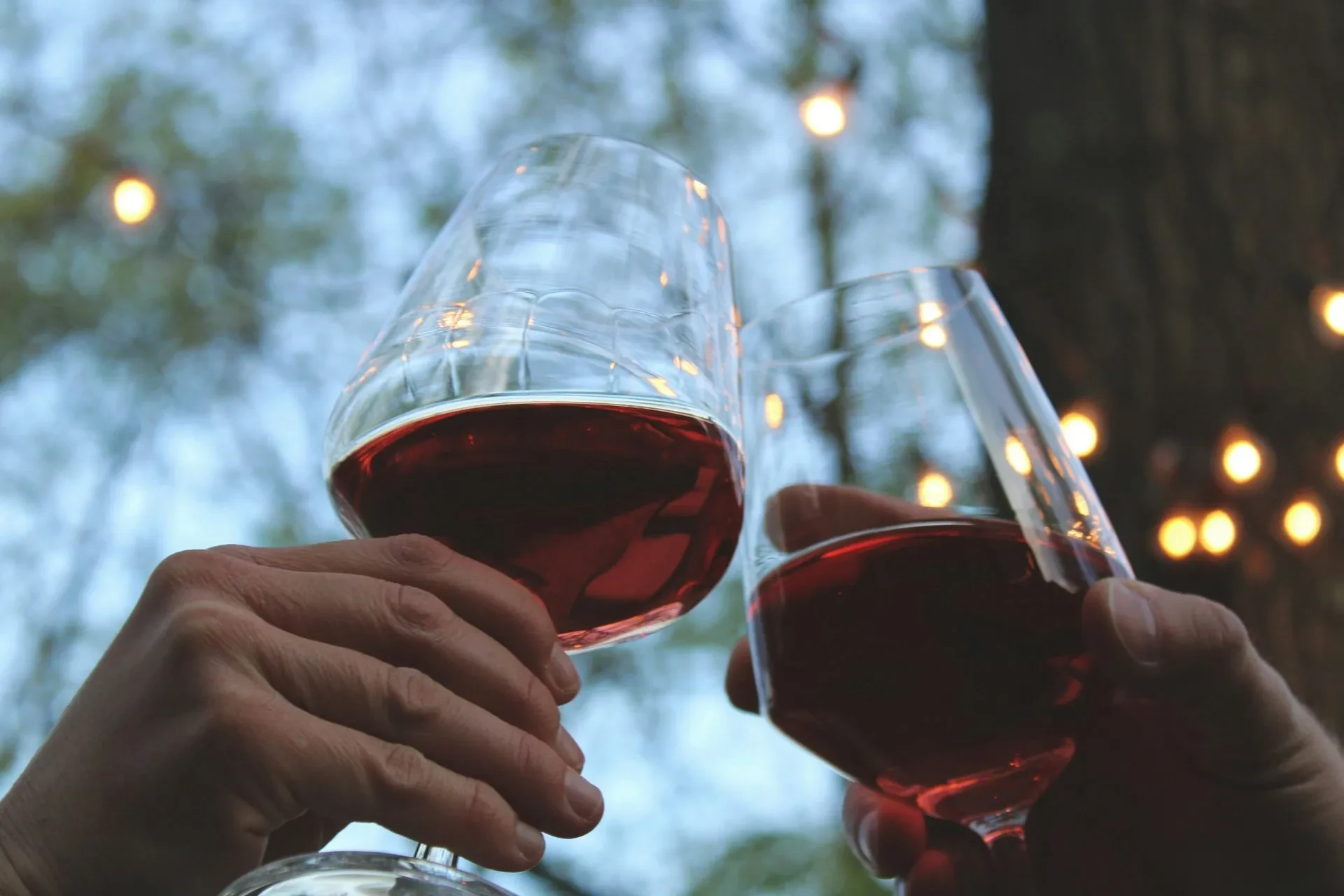 Two glasses of red wine clinking outdoors.